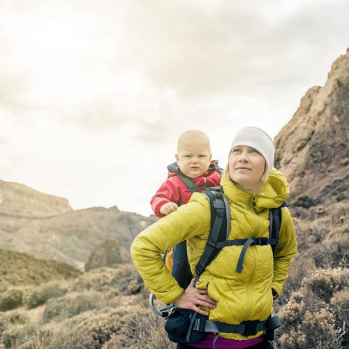 Superhero mother with little boy travelling in backpack. Hiking adventure with child on family trip in mountains. Vacations journey with infant carried on back, weekend travel in Tenerife, Spain.